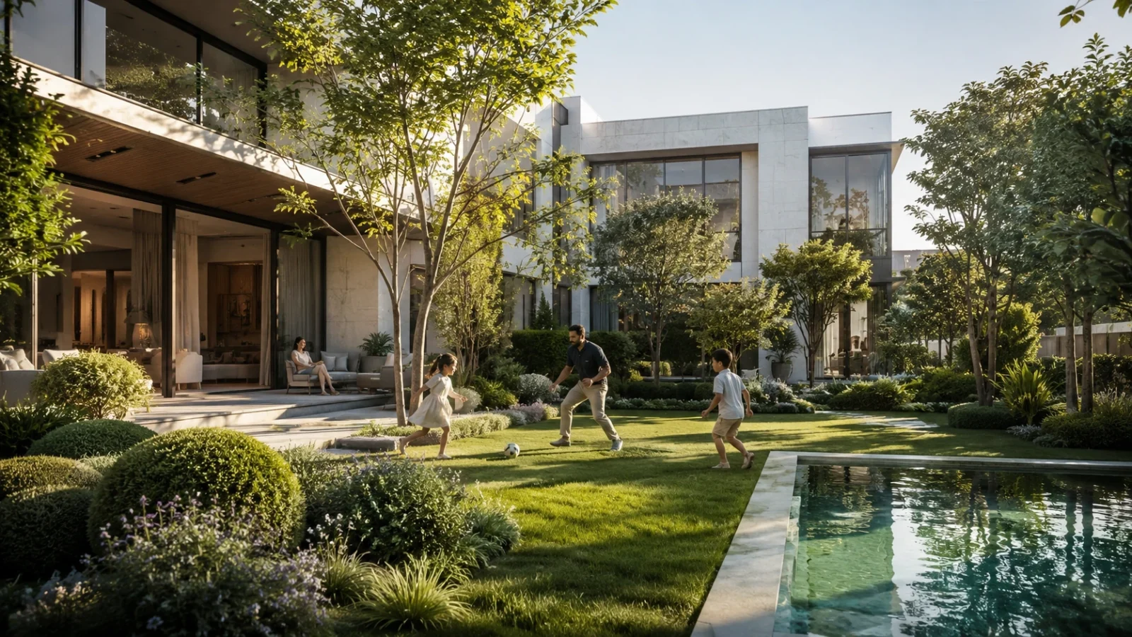 A landscaped villa garden with a lawn and pool beside open glazed living areas in warm evening light